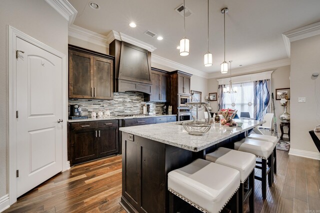 kitchen featuring custom exhaust hood, an island with sink, hanging light fixtures, and dark hardwood / wood-style flooring