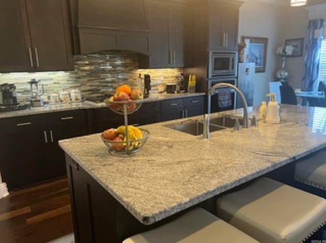 kitchen featuring custom range hood, dark brown cabinets, sink, and light stone counters