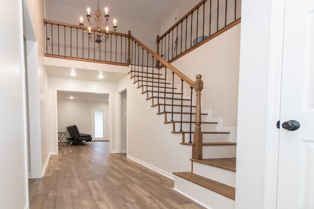 stairway featuring wood-type flooring, a chandelier, and a towering ceiling