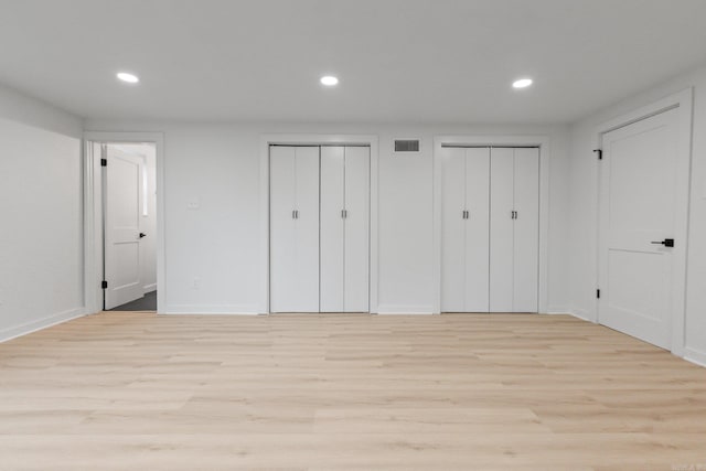 unfurnished bedroom with two closets and light hardwood / wood-style floors