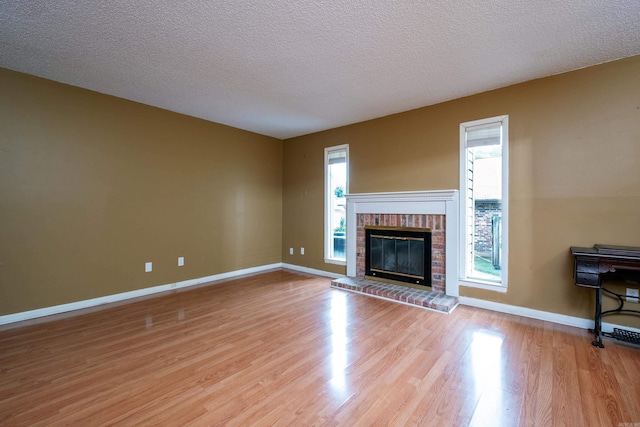 unfurnished living room featuring a textured ceiling, light wood-type flooring, and a brick fireplace