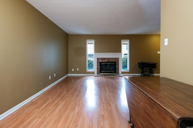 unfurnished living room featuring a textured ceiling, light hardwood / wood-style flooring, and a brick fireplace