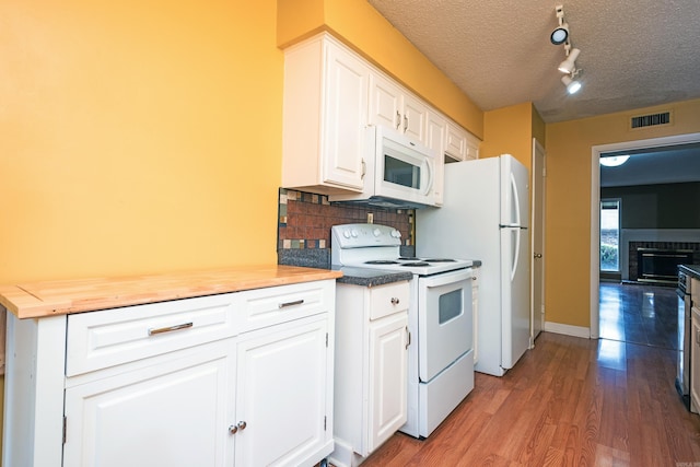 kitchen featuring white cabinets, hardwood / wood-style flooring, a brick fireplace, white appliances, and a textured ceiling