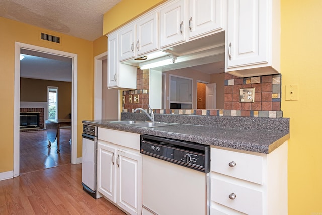 kitchen featuring a textured ceiling, dishwasher, sink, white cabinets, and light hardwood / wood-style floors