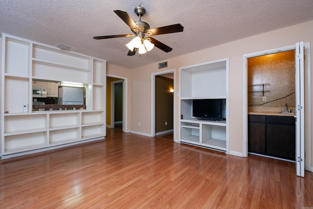 unfurnished living room featuring ceiling fan, hardwood / wood-style flooring, sink, and a textured ceiling