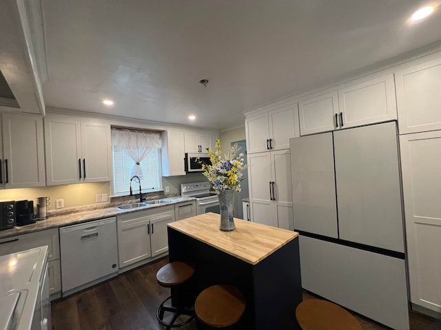 kitchen with a kitchen island, dark hardwood / wood-style floors, white appliances, sink, and white cabinets