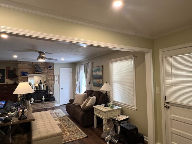 living room with ornamental molding, dark wood-type flooring, ceiling fan, and a stone fireplace