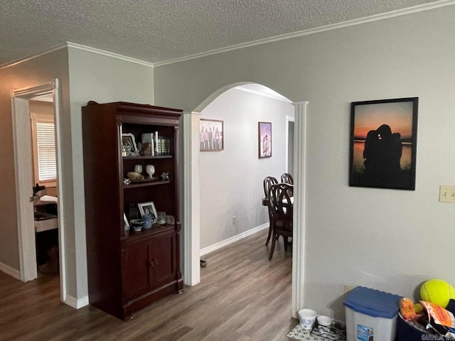 corridor featuring wood-type flooring, ornamental molding, and a textured ceiling