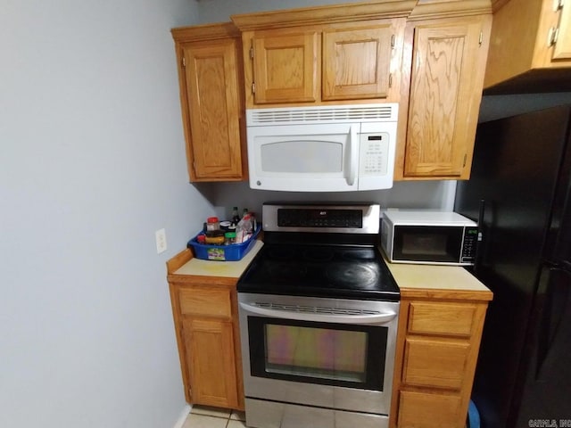 kitchen with light tile patterned floors, black fridge, and stainless steel range with electric cooktop