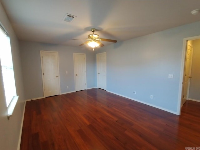 unfurnished bedroom featuring multiple closets, dark wood-type flooring, and ceiling fan