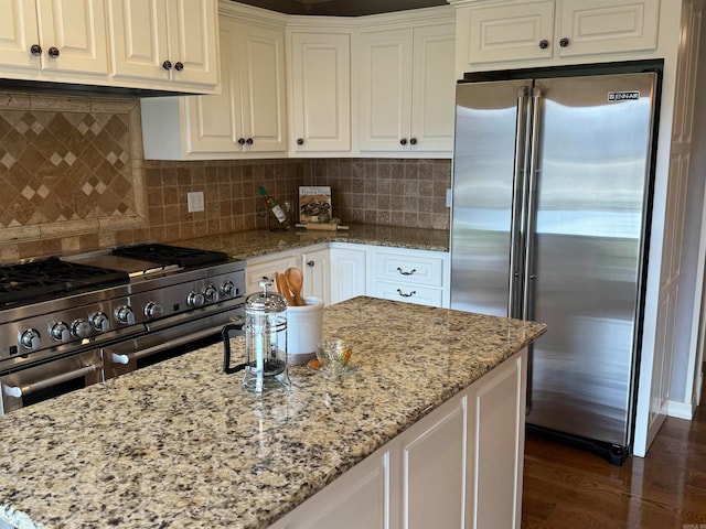 kitchen featuring high end appliances, tasteful backsplash, light stone countertops, dark hardwood / wood-style floors, and white cabinets