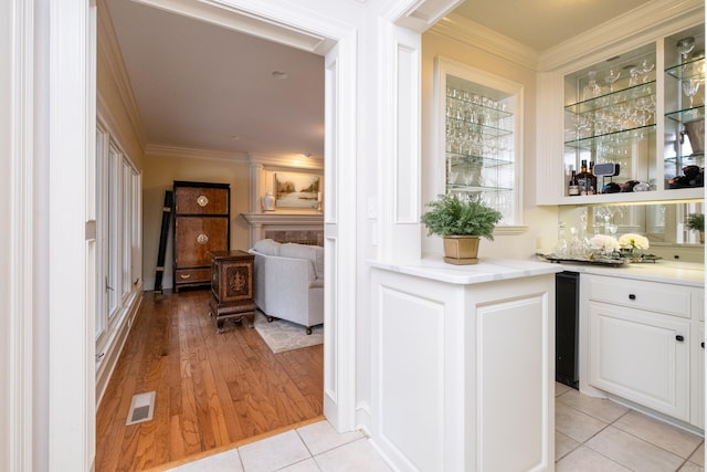 bar featuring ornamental molding, beverage cooler, white cabinets, and light hardwood / wood-style floors