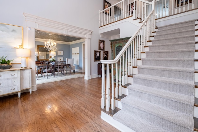 stairs with a towering ceiling, ornamental molding, hardwood / wood-style flooring, and a notable chandelier