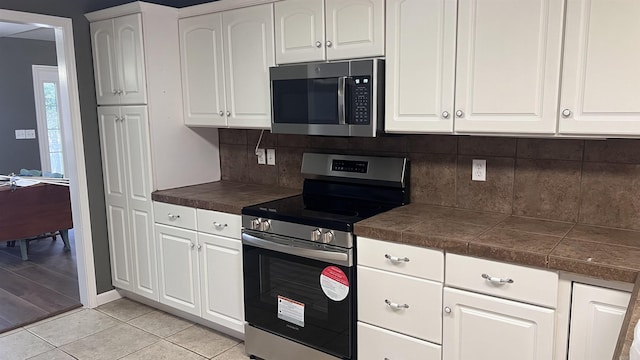 kitchen featuring light tile patterned floors, baseboards, decorative backsplash, white cabinets, and appliances with stainless steel finishes