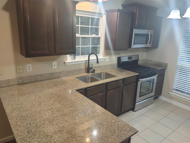 kitchen with dark brown cabinetry, light tile patterned flooring, sink, appliances with stainless steel finishes, and light stone countertops