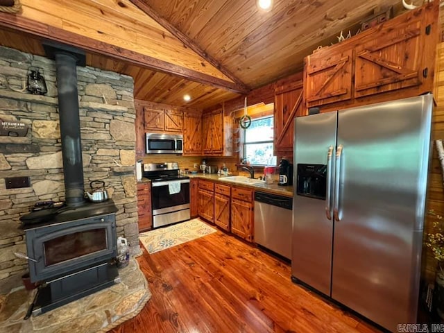 kitchen featuring light hardwood / wood-style floors, sink, a wood stove, vaulted ceiling, and stainless steel appliances