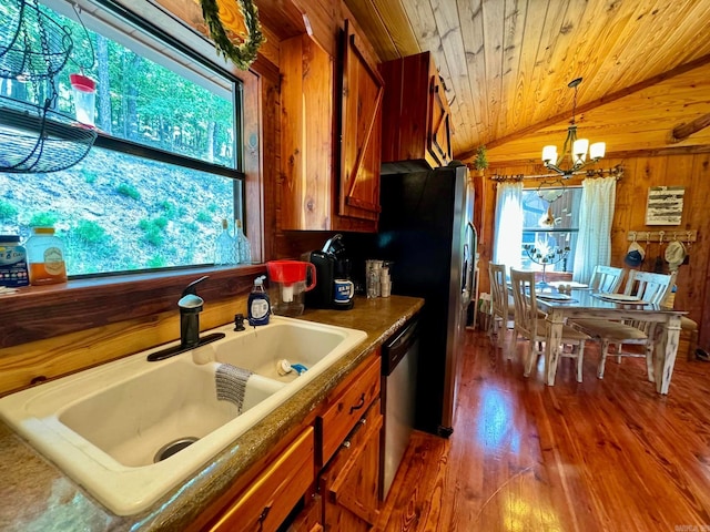 kitchen with wood walls, dishwasher, wood-type flooring, an inviting chandelier, and sink