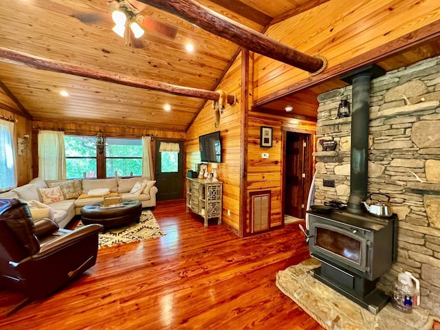 living room featuring a wood stove, wood walls, vaulted ceiling with beams, hardwood / wood-style floors, and ceiling fan