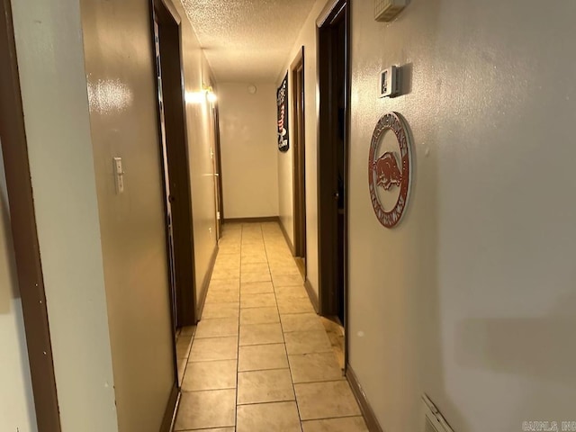 hallway with a textured ceiling and light tile patterned floors