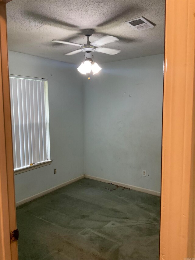 empty room featuring a textured ceiling, ceiling fan, and dark colored carpet