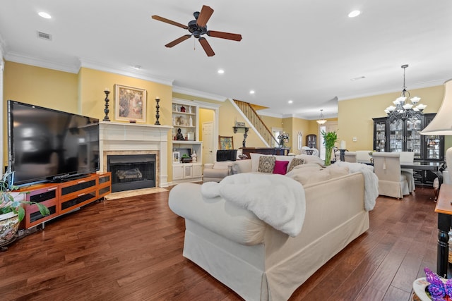 living room with ornamental molding, a tiled fireplace, dark hardwood / wood-style floors, and ceiling fan with notable chandelier