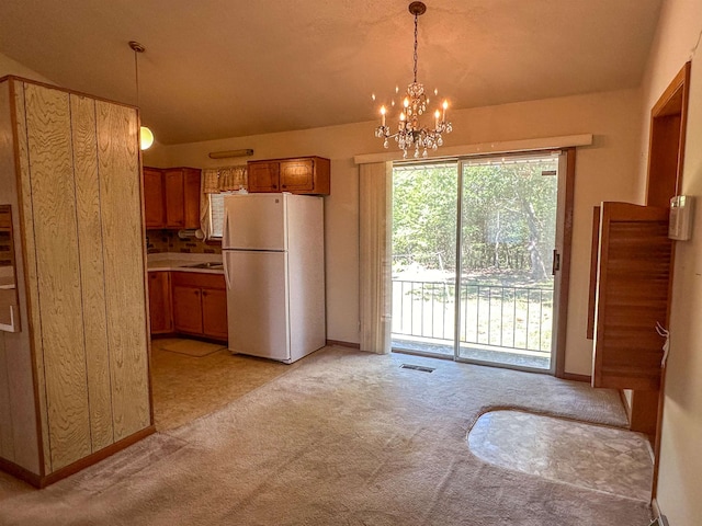 kitchen with an inviting chandelier, pendant lighting, light colored carpet, and white refrigerator