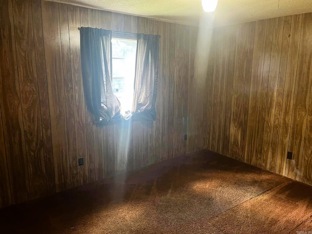 carpeted empty room with wood walls and a textured ceiling