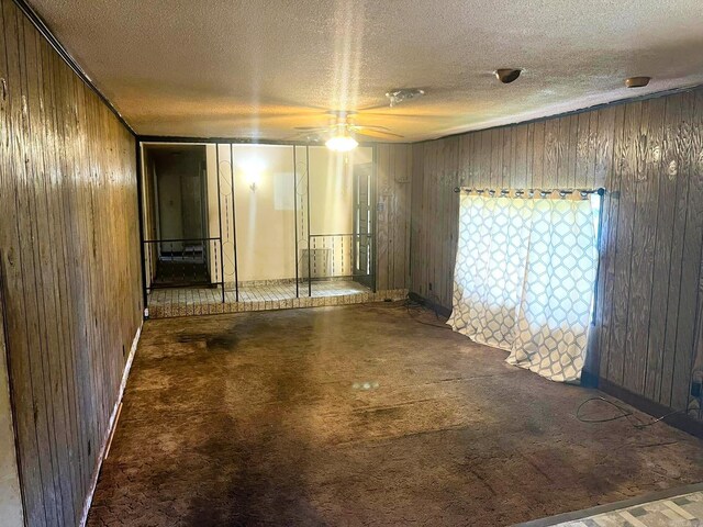 empty room with a textured ceiling, carpet flooring, wooden walls, and ceiling fan