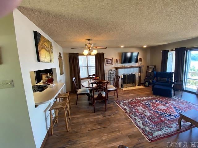 dining room featuring ceiling fan, hardwood / wood-style flooring, a tile fireplace, and a textured ceiling