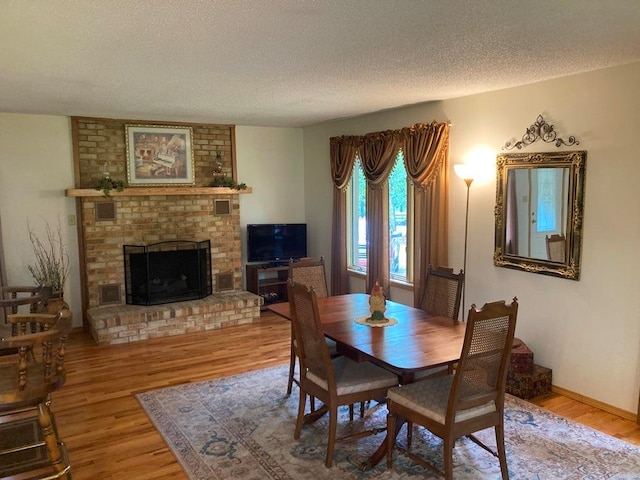 dining room featuring a brick fireplace, a textured ceiling, and hardwood / wood-style flooring