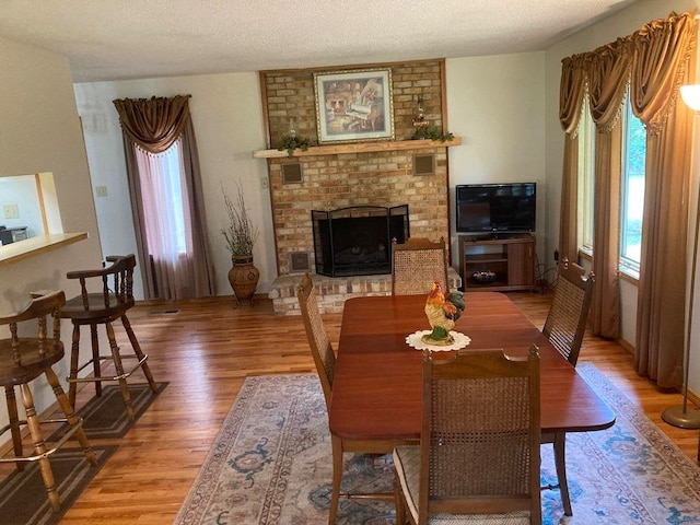 dining room with a textured ceiling, wood-type flooring, and a fireplace