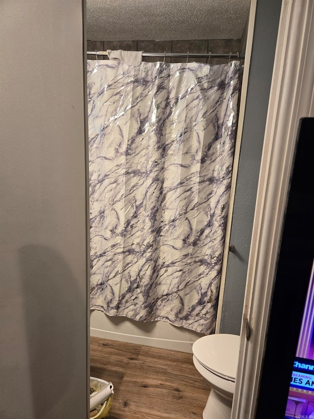 bathroom featuring shower / tub combo with curtain, a textured ceiling, hardwood / wood-style flooring, and toilet