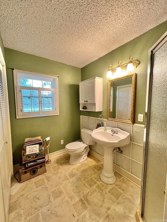 bathroom with a textured ceiling, sink, toilet, and a shower with door