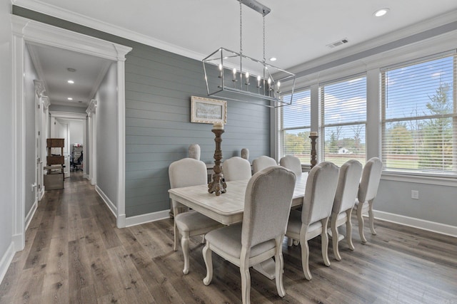 dining room with crown molding, wood-type flooring, wood walls, and a chandelier