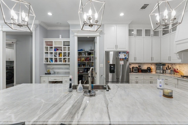 kitchen featuring decorative backsplash, a chandelier, light stone counters, and stainless steel fridge