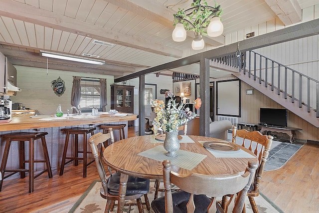 dining space featuring wooden walls, beam ceiling, light hardwood / wood-style floors, and wooden ceiling