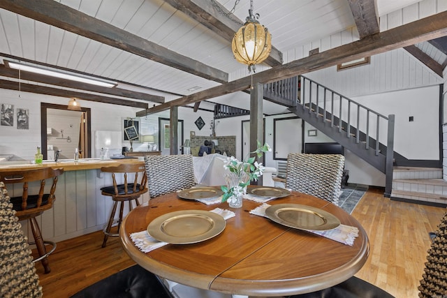 dining area featuring wood-type flooring, beamed ceiling, and wood walls