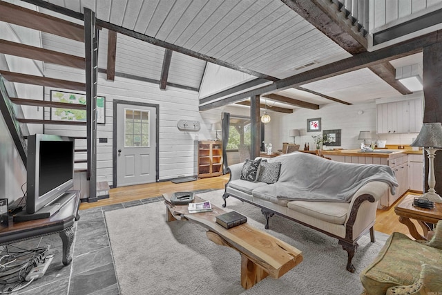 living room with lofted ceiling with beams, light hardwood / wood-style floors, wood walls, ceiling fan, and wooden ceiling