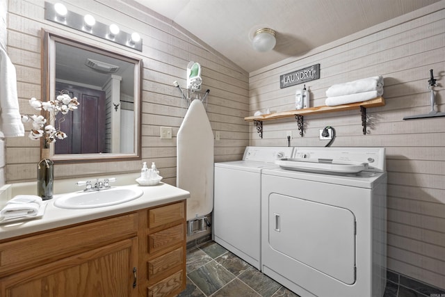 laundry area featuring wooden walls, sink, and washing machine and dryer