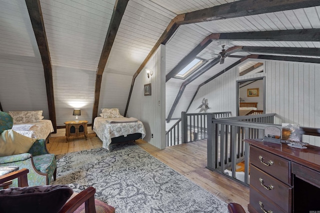 bedroom with lofted ceiling with skylight, wood walls, and light hardwood / wood-style flooring