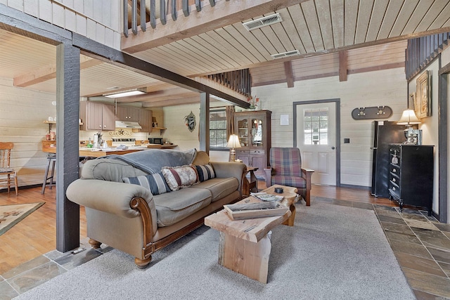 living room with beamed ceiling, wooden walls, hardwood / wood-style floors, and a healthy amount of sunlight