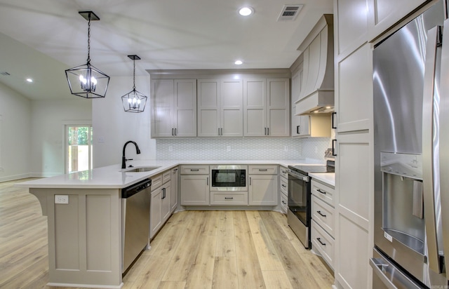 kitchen featuring hanging light fixtures, sink, kitchen peninsula, appliances with stainless steel finishes, and light hardwood / wood-style floors