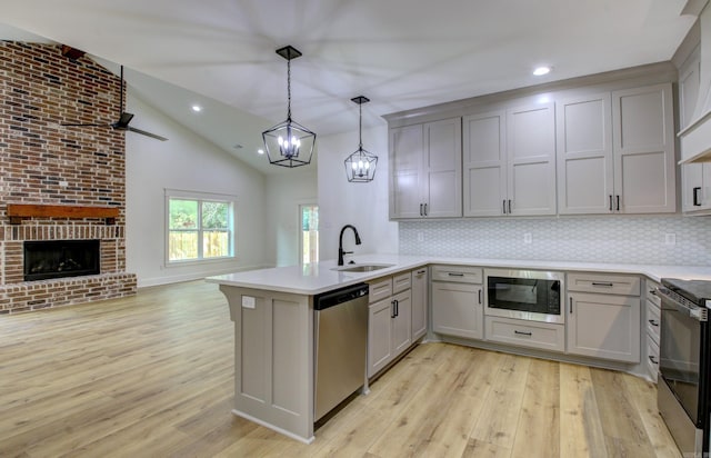 kitchen featuring hanging light fixtures, sink, kitchen peninsula, a brick fireplace, and appliances with stainless steel finishes