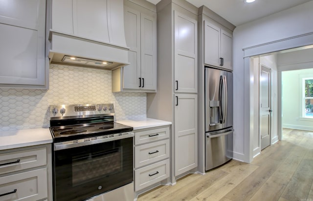 kitchen with light wood-type flooring, appliances with stainless steel finishes, backsplash, and custom range hood