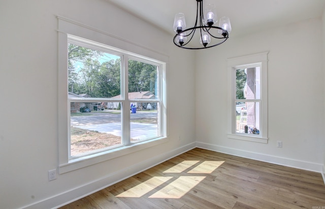 spare room with light hardwood / wood-style flooring, a notable chandelier, and plenty of natural light