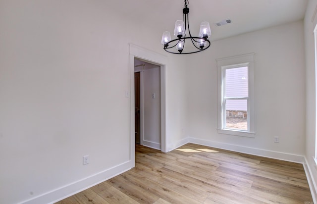 spare room featuring an inviting chandelier and light hardwood / wood-style flooring