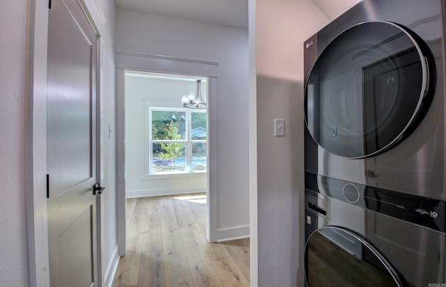 clothes washing area with light hardwood / wood-style floors, stacked washer / dryer, and a chandelier