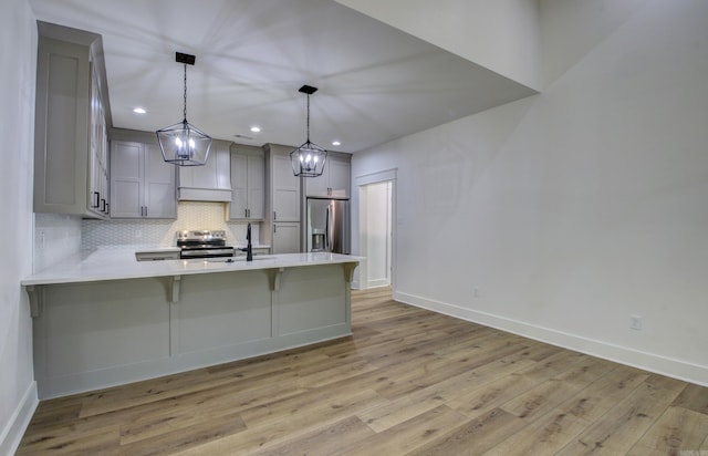 kitchen with light wood-type flooring, kitchen peninsula, hanging light fixtures, a kitchen breakfast bar, and appliances with stainless steel finishes