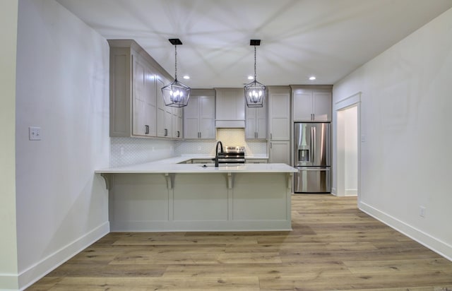 kitchen with backsplash, kitchen peninsula, pendant lighting, stainless steel appliances, and light wood-type flooring