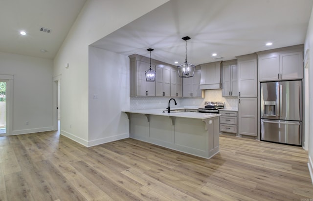 kitchen featuring light hardwood / wood-style floors, lofted ceiling, custom exhaust hood, stainless steel appliances, and decorative light fixtures